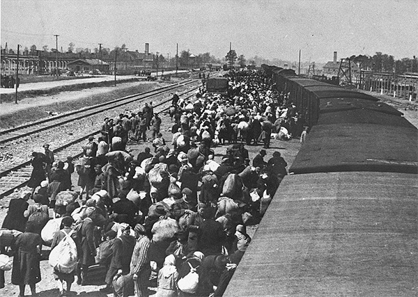 Grupos de judíos llegando en trenes al campo de concentración de Auschwitz. Al fondo pueden verse las chimeneas de los crematorios de cadáveres.